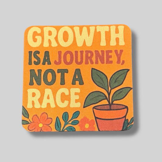 Inspirational orange coaster with a plant in a pot and the quote “Growth is a journey, not a race.